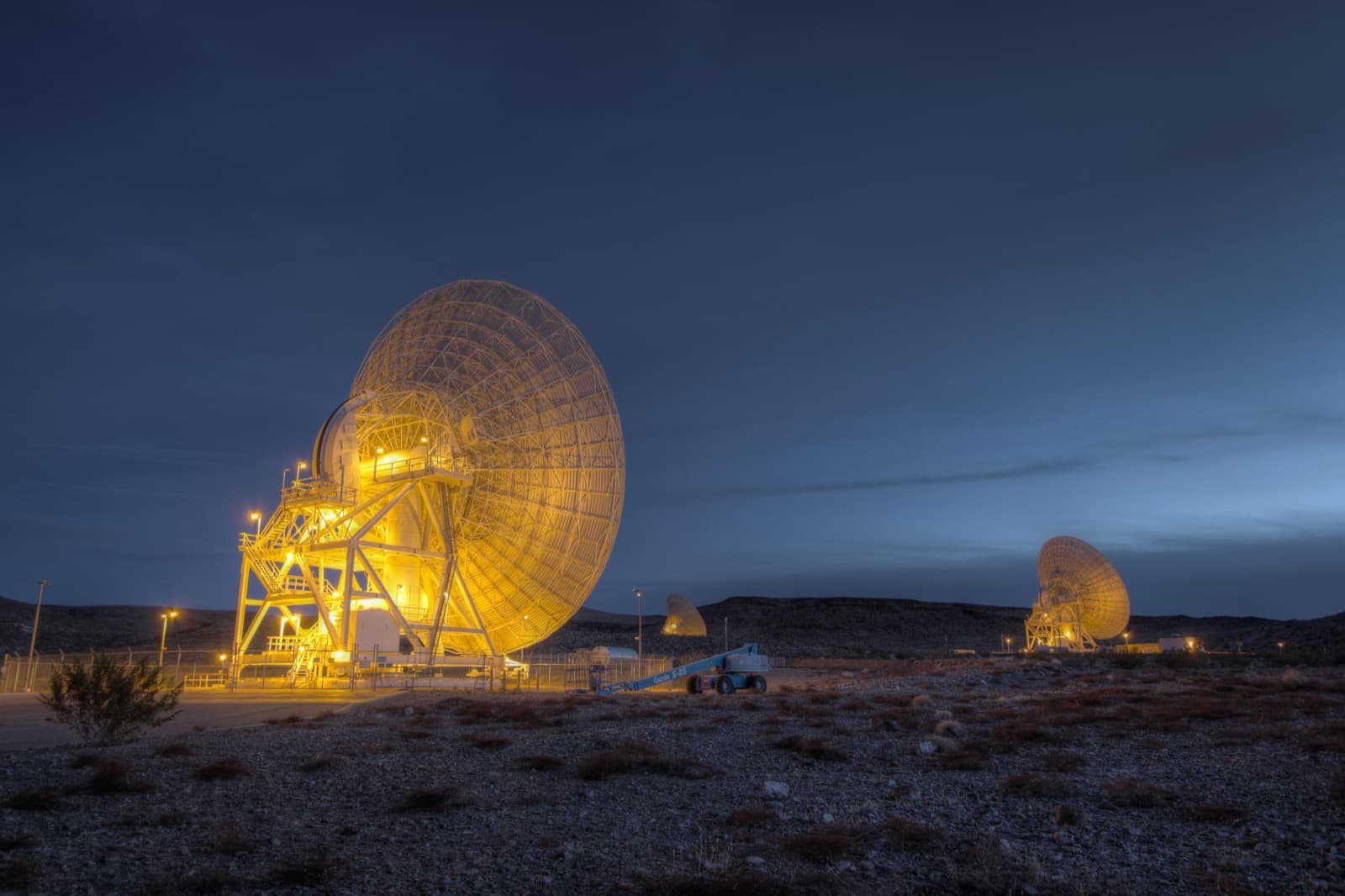 Three large Deep Space Network dish antennas at the Goldstone complex, lit against the night sky